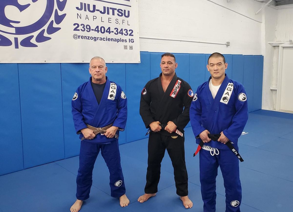 Three Renzo Gracie Naples black belts standing on the mat in front of the academy wall
